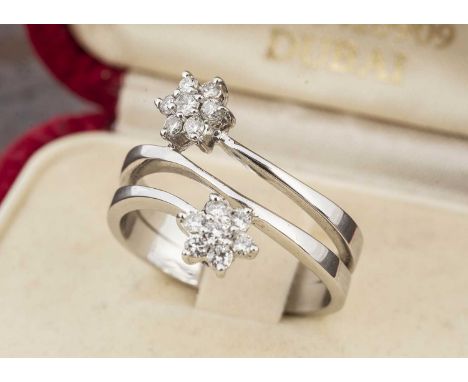 A continental white metal 750 marked crossover dress ring, the diamond clusters in claw settings on a double band shank, ring