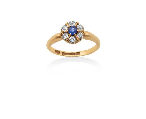 An 18 Carat Gold Sapphire and Diamond Cluster Ringthe round cut sapphire within a border of old cut diamonds spaced by yellow