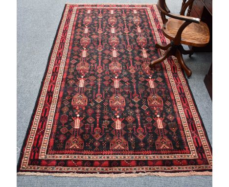 Baluch Rug, the charcoal field with an allover design of urns and candelabra, framed by borders of geometric motifs, flanked 