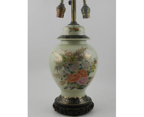A Japanese two armed table lamp base, decorated with flowers and foliage highlighted in gilt, mounted on a carved wooden base