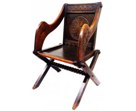 A late Victorian carved oak Glastonbury elbow chair with decorative back rail, shaped armrests and X-frame base with bobbin s