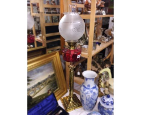 A brass Corinthian column oil lamp with cranberry glass font and later shade.