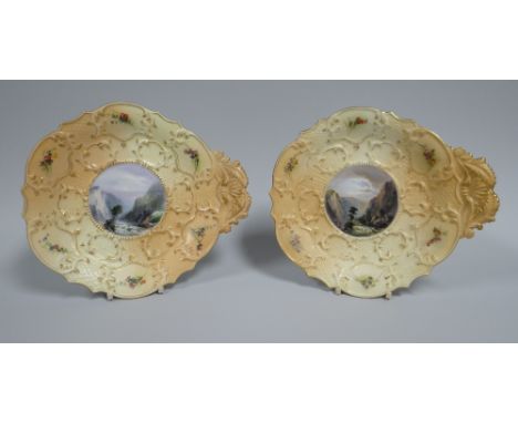 A PAIR OF ROYAL WORCESTER DISHES moulded with foliate handles and foliate borders featuring painted centre cameos of river sc