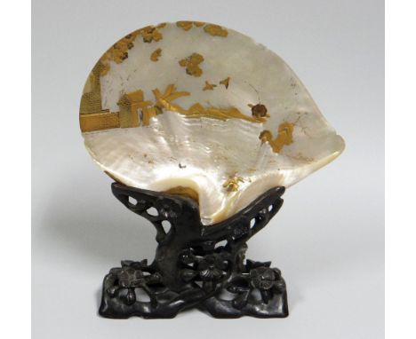 A JAPANESE MOTHER-OF-PEARL TABLE-SCREEN on a naturalistic carved hardwood stand, the shell gold painted with a partial buildi