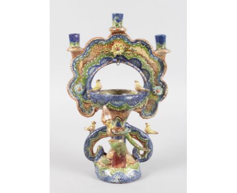 A FOLK ART POTTERY CANDLESTICK painted in brilliant colours and birds. 11ins high.