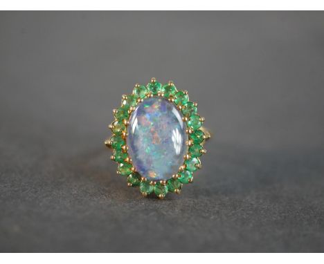 A 9 carat yellow gold black opal triplet and emerald cluster dress ring. Set to the centre with an oval black opal triplet su