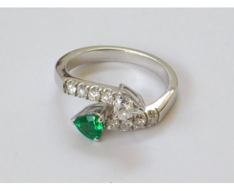 EMERALD RING. An 18ct. white gold emerald & diamond cross-over ring, each terminal set a heart shaped stone. Approx. 5.1g. Si