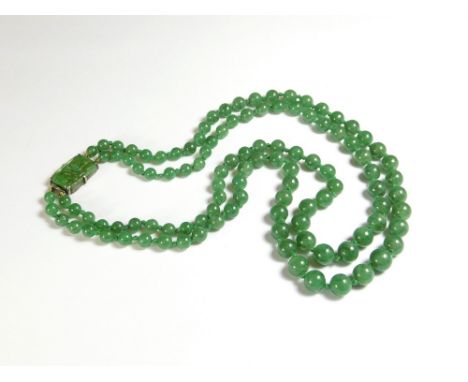 JADE NECKLACE. A twin strand, knotted, graduated jade bead necklace with carved jade set clasp.  Please note that all items i