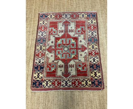 A red ground rug with a repeating Aztec pattern 123cm x 100cm 