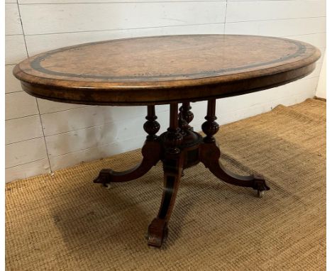 An oval walnut centre table with ebonised inlay and pierced floral detail, on four splayed legs with fluted column supports a
