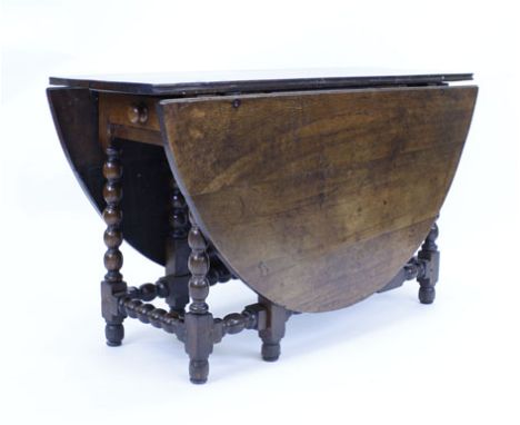An 18th century and later oak gateleg dining table with a single frieze drawer on bobbin turned supports joined by stretchers