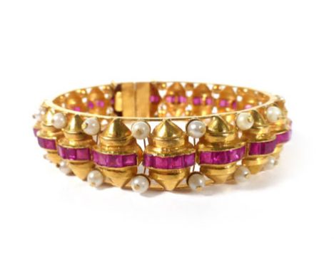 An Indian yellow metal bangle set small pearls and square cut synthetic rubies within channel type settings raised on ninetee