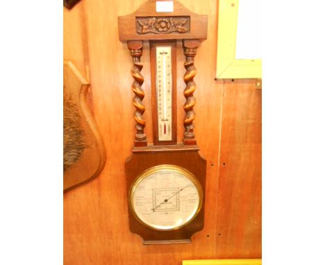 A 1930's oak cased barometer and thermometer surmounted with a floral carved panel over barley twist supports 