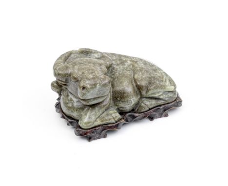 A LARGE GREEN AND RUSSET JADE WATER BUFFALOFormed from a large green nephrite boulder, the recumbent animal with his legs tuc