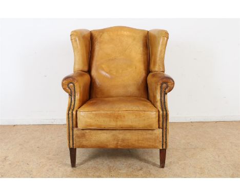 Cognac lederen oorfauteuil afgezet met siernagels, rustend op houten poten.