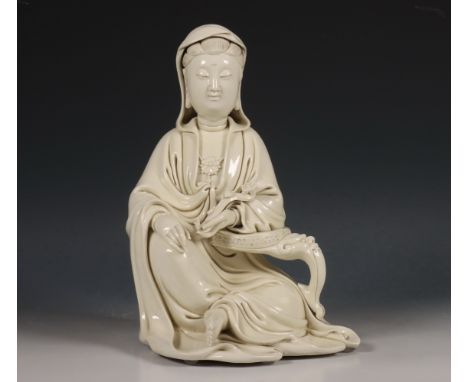 China, Dehua porseleinen Guanyin, 20e eeuw, gemodelleerd in zittende positie leunend op een tafeltje met maskerkop, gekleed i