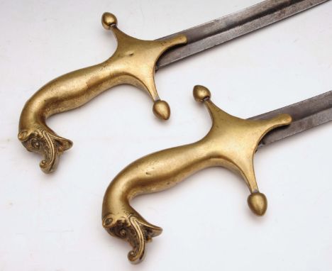 A PAIR OF ANTIQUE STEEL SWORDS with curved blades and brass handles with mythological creature finial, probably Middle Easter