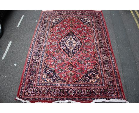 A PERSIAN RED GROUND SMALL CARPET, the central foliate medallion within a field of scrolling flowers and a triple border, 286