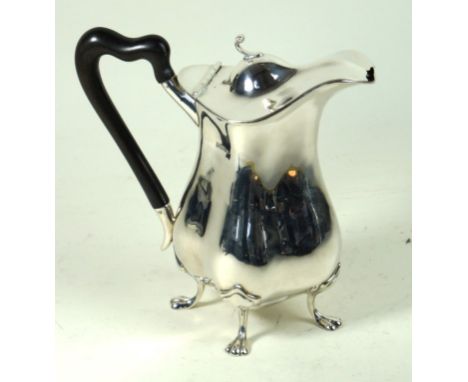 An Edwardian silver hot water pot
Of wavy baluster form, the hinged dome lid with a scroll finial, to an ebonised handle, rai