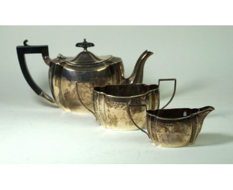 A silver three piece tea service
Of plain oval form, with inverted panels, the tea pot with an ebonised finial and angular ha