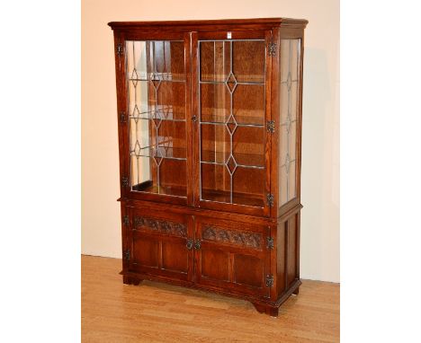  An Old Charm oak display cabinet, with two leaded glazed doors enclosing glass shelved interior, and interior light, above t