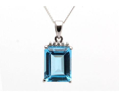 A gorgeous emerald cut blue topaz gemstone is set with  five round brilliant cut diamonds resting on the blue topaz in this 9