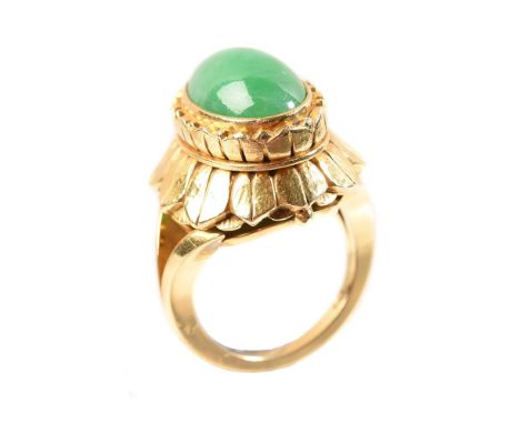 
	
		A jadeite and gold coloured dress ring, the oval cabochon jadeite panel within a petal like surround with lightly hammer