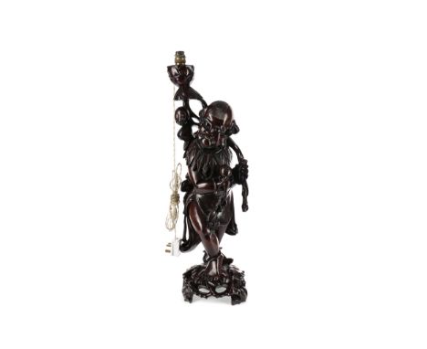 EARLY 20TH CENTURY CHINESE HARDWOOD FIGURAL LAMP, carved as a male figure holding a fruit in his right hand and stood on a pi