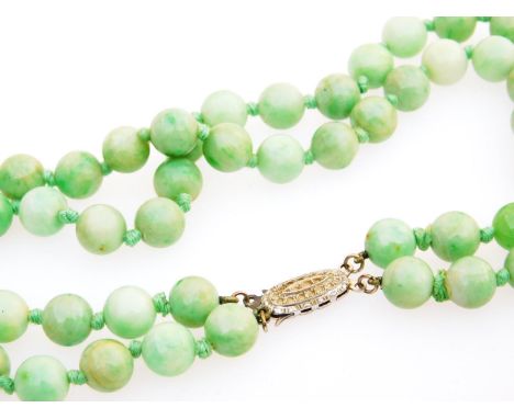An early 20thC polished jade necklace, set with light green uniform beads with central fancy clasp in two strands, plain stri