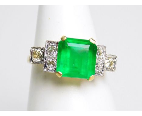 An 18ct emerald and diamond Art Deco style ring, the claw set central stone flanked by three diamonds to each shoulder, with 