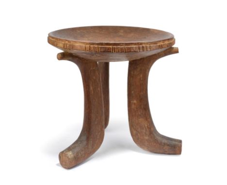 A Jimma stool Ethiopia with a carved edge to the dipped seat and on three scroll legs, 40.5cm high, 41cm diameter.