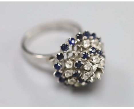 A white metal (stamped 18k) and two colour sapphire? set raised cluster ring, size K/L, gross 5.2 grams (one stone missing).