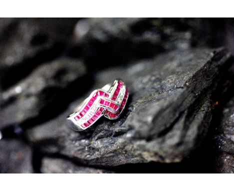 A ruby and diamond dress ring, designed as a ruby and diamond set ribbon 'twist', all set in white metal stamped '750', total