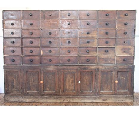 A 19th century apothecary bank of drawers, with forty two drawers with turned handles, some with paper labels, on base with s