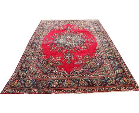 A Persian Tabriz wool carpet, worked with a central floral medallion and corner spandrels, against a red ground, 375cm x 202c