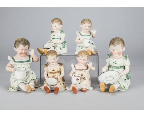 Three pairs of German bisque children with cups and saucers,  all seated, one holding a saucer and one holding a tea cup, two