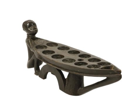 A WOODEN 'MANCALA' GAMING BOARD possibly Mbala, Republic of Congo, with seated figure supporting with his hands the long ovoi