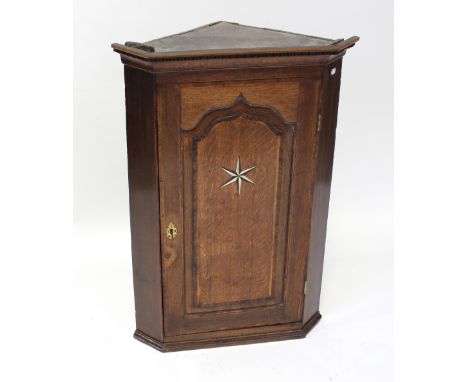 A George III oak panel hanging corner cabinet, cross-banded in mahogany with inlaid bog oak and bone star paterae, pointed ar