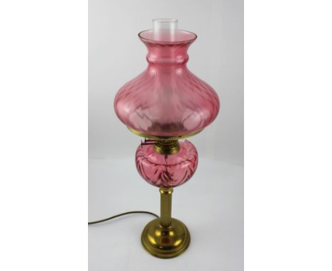 An early 20th century cranberry glass and brass paraffin lamp converted to electricity, with later pink flashed shade and smo