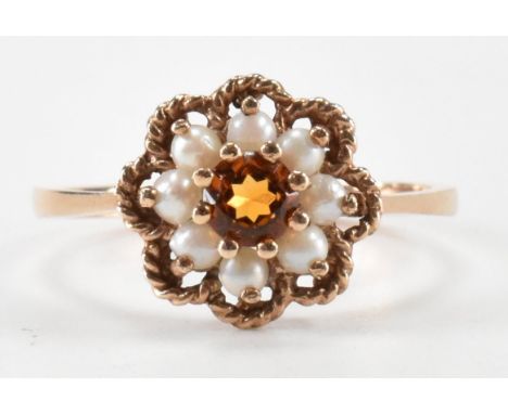 A hallmarked 9ct gold citrine and pearl cluster ring. The ring having a flower head with a central round cut citrine and a ha