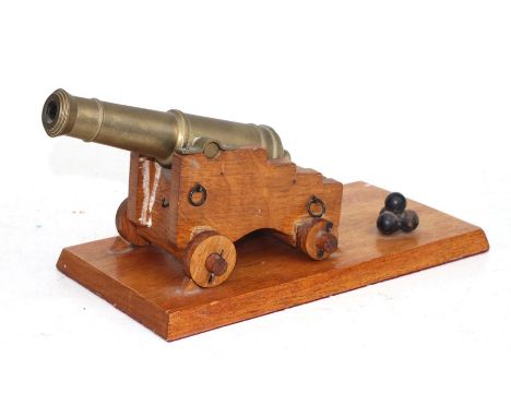 A desk top cannon with a brass barrel mounted on a wooden carriage with brass &amp; metal fittings, sitting on a hardwood pli