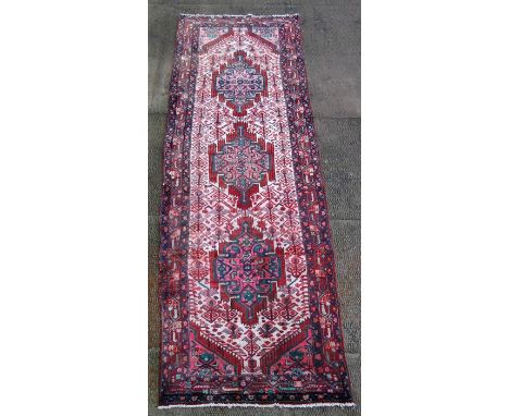 A Persian Hamedan woollen hand knotted runner with three repeated guls within stylised borders on a cream &amp; red ground, 3