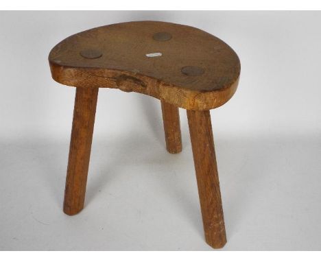 A Robert Mouseman Thompson oak cow stool with kidney shaped top and octagonal tapered supports, carved signature mouse, appro