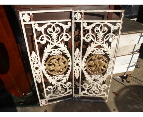 Two white painted cast iron gate frames, each with pierced decoration each with a cherub  