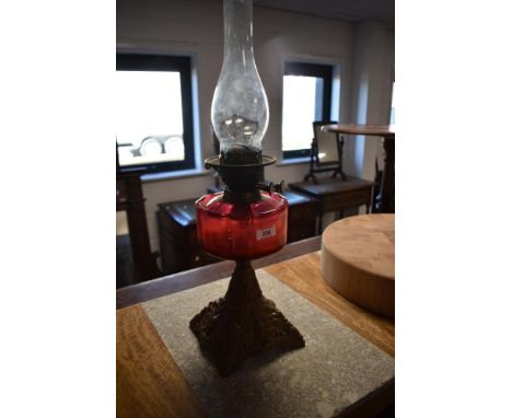 A Victorian cast-metal and cranberry glass oil lamp, the cranberry glass reservoir raised on a cast and gilt painted metal ba