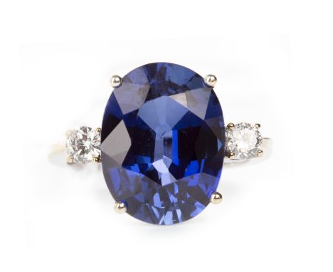 BLUE GEM SET AND DIAMOND RINGset with an oval blue created sapphire 15.2mm long, flanked by two round brilliant cut diamonds 