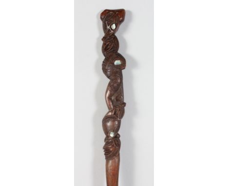 A MAORI TOKO TOKO CHIEFS STICK, the upper part carved with stylised figures and masks with shell inlaid eyes. 35.5ins long.