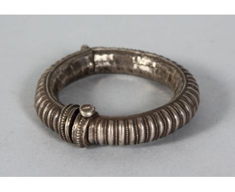 AN EASTERN WHITE METAL BANGLE, with ribbed decoration. 3.5ins diameter.