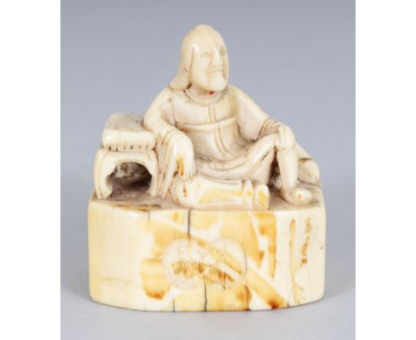 A GOOD 18TH CENTURY JAPANESE EDO PERIOD IVORY NETSUKE, carved in the form of a man reclining against a low table, the front o