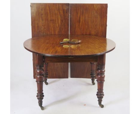 19th century mahogany extending circular dining table, raised on ring turned and tapering legs terminating in casters, includ